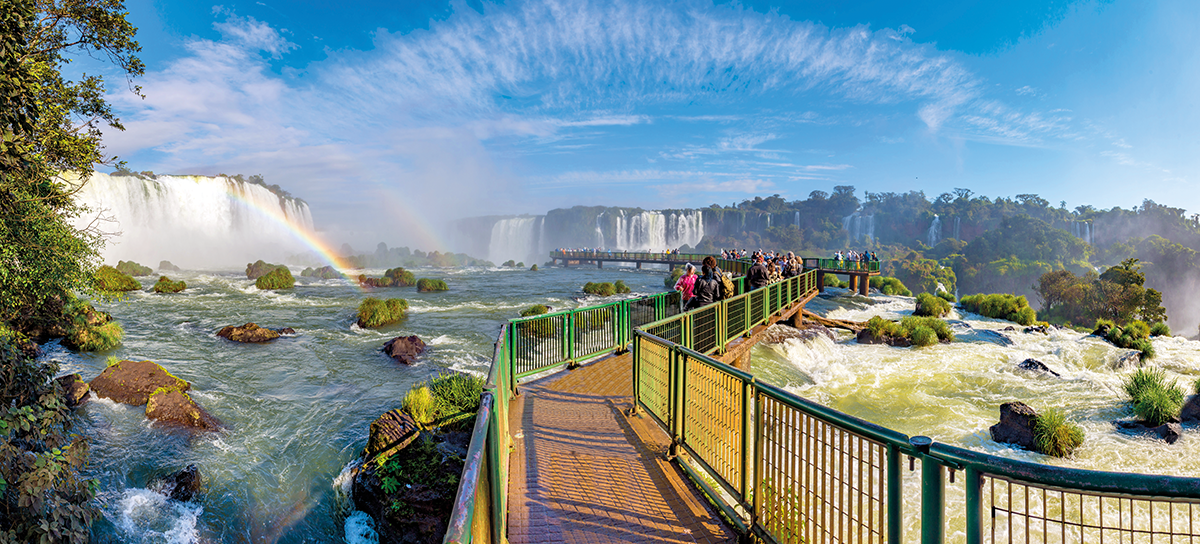 ponte sobre as águas das cataratas do iguaçu, céu ensolarado, arco-iris, pessoas andando na ponte