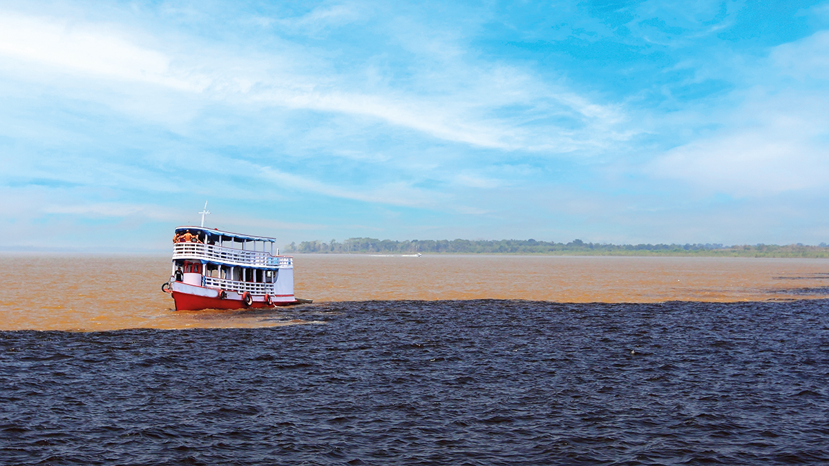 barco navegando no encontro entre os rios negro de água escura e Solimões de água marrom claro