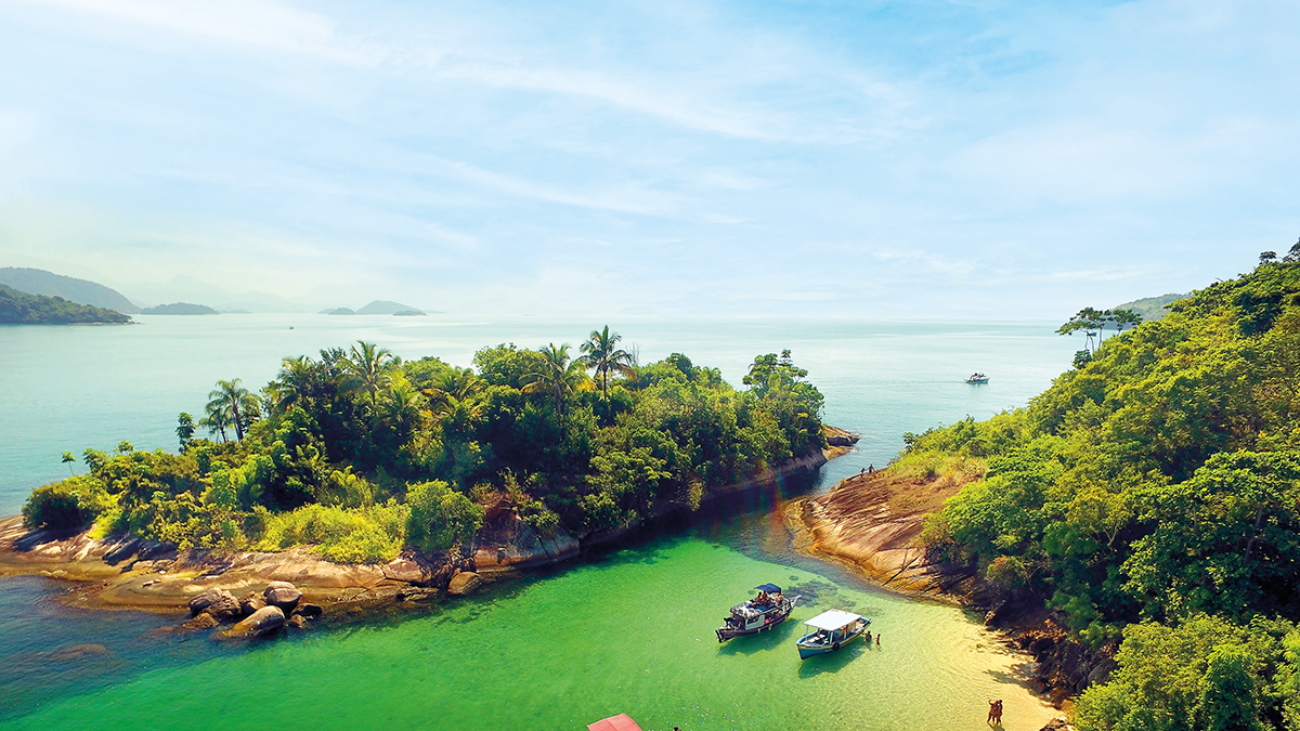 paisagem com céu azul e abaixo a ilha com árvores verdes e alguns barcos na água cristalina