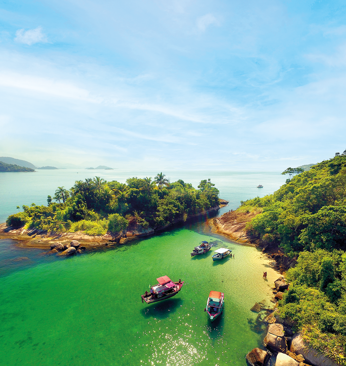 paisagem com céu azul e abaixo a ilha com árvores verdes e alguns barcos na água cristalina