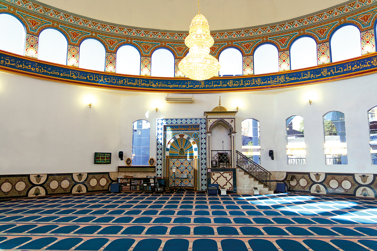 interior da mesquita, com piso azul e ilustrações e escritas nas paredes, ao centro um lustre