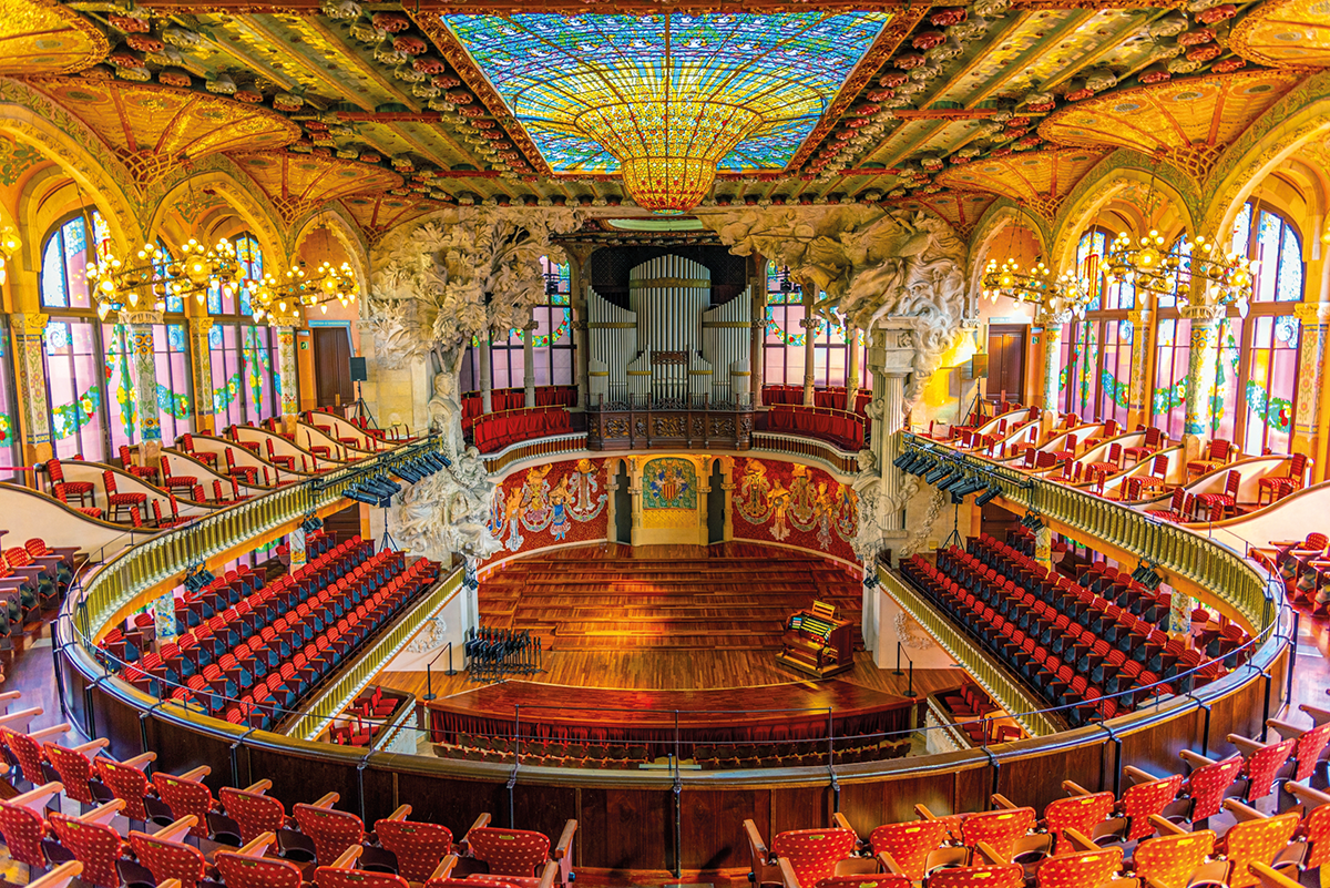 interior de um teatro com arquibancadas, cadeiras vermelhas em 3 andares diferentes, ao centro o palco, no teto vitrais, lustres e ilustrações decorativas