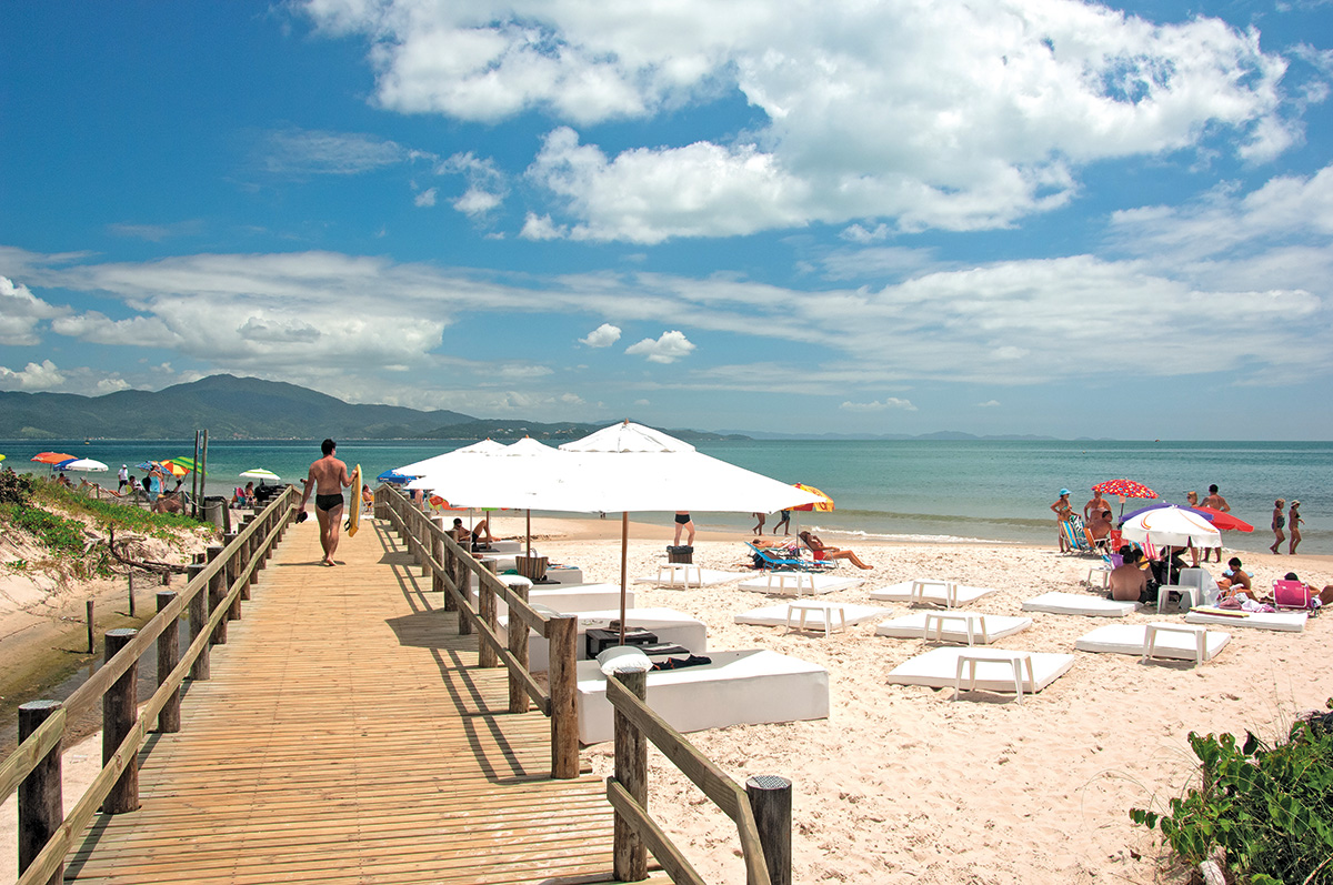 Um deck na Praia dos Ingleses e ao fundo alguns gurda-sóis e cadeiras brancas.