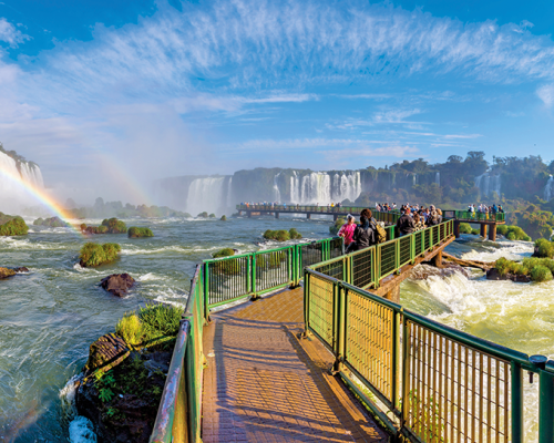 ponte sobre as águas das cataratas do iguaçu, céu ensolarado, arco-iris, pessoas andando na ponte