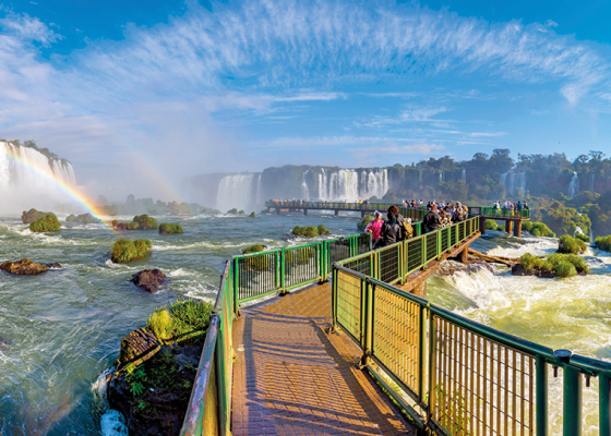 ponte sobre as águas das cataratas do iguaçu, céu ensolarado, arco-iris, pessoas andando na ponte