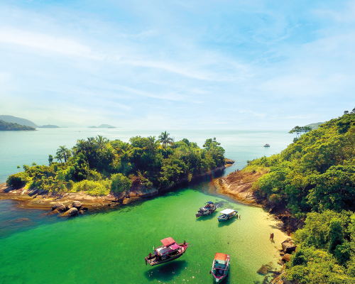 paisagem com céu azul e abaixo a ilha com árvores verdes e alguns barcos na água cristalina