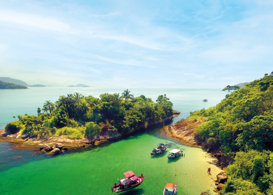 paisagem com céu azul e abaixo a ilha com árvores verdes e alguns barcos na água cristalina